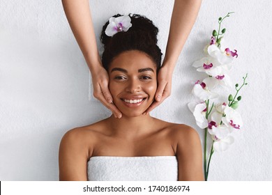 Aesthetic Procedure. Beautician Making Face Massage For Smiling Black Woman, Top View