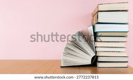 Aesthetic stack of books with one open book placed on a wooden table against a soft pastel pink background. Minimalist composition with ample copy space, ideal for education, reading, knowledge concepts, or lifestyle themes. Clean and modern visual with negative space perfect for text overlay, banners, or social media content.