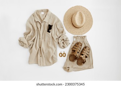 Aesthetic summer fashion composition with neutral beige female clothes and accessories. Muslin tee blouse, shorts, straw hat, leather sandals, sunglasses, earrings. Flat lay, top view.