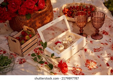 Aesthetic Summer Picnic In The Sunny Garden. Pink Tablecloth, Box Of Marshmallows, Strawberries, Cherry, Peas And Glasses Of Wine Among Pink Roses. Romantic Evening, Appreciation Of The Moment