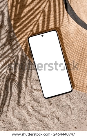 Aesthetic tropical summer business branding template, mobile phone empty screen mockup, straw hat on sand beach texture background with natural palm tree foliage sunlight shadow.
