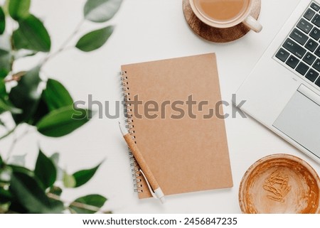 Aesthetic workspace, top view. Notepad, laptop, coffee and office supplies with green leaves. Cozy home office desk, work, freelance, creative workplace