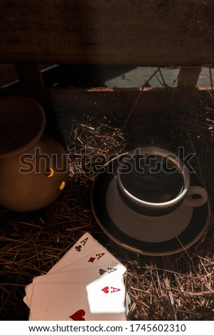 Aesthetically pleasing photo with coffee cup , playing cards and a candle lamp . 
