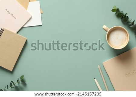 Aesthetics minimal workspace with paper notebooks, coffee cup, eucalyptus leaves on green table. Flat lay, top view