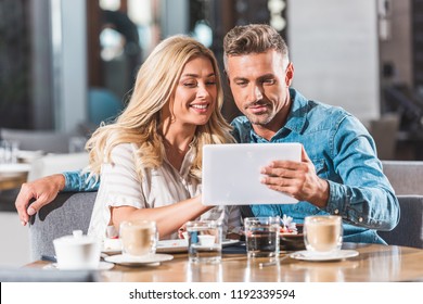 affectionate adult couple using tablet at table in cafe