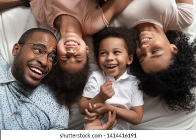 Affectionate African American Parents And Cute Small Kids Laughing Lying On Bed Together, Happy Mixed Race Family With Children Bonding Having Fun Enjoy Funny Moments In Bedroom, Top View From Above