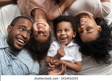 Affectionate african american parents and cute small kids laughing lying on bed together, happy mixed race family with children bonding having fun enjoy funny moments in bedroom, top view from above - Powered by Shutterstock