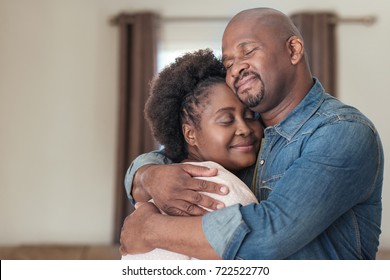 Affectionate African couple smiling and hugging each other while standing together with their eyes closed in their living room at home