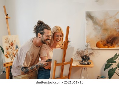 An affectionate artistic couple is standing at creative art studio and painting together on easel. Romantic creative couple is hugging while standing at atelier and painting on canvas together. - Powered by Shutterstock