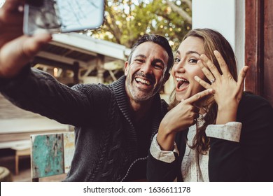 Affectionate couple announcing their engagement with selfies while sitting at cafe. Happy couple taking a selfie and showing off their wedding ring at coffee shop. - Powered by Shutterstock