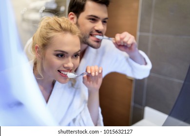 Affectionate Couple Brushing Teeth And Looking At Mirror