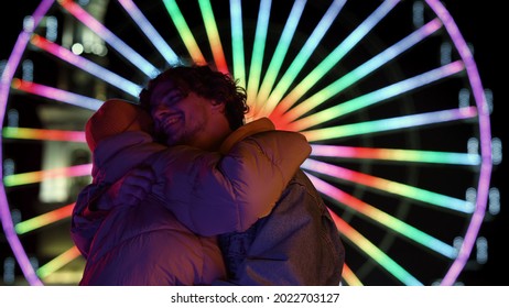 Affectionate Couple Hugging On Urban Street At Night. Happy Man And Woman Dating Against Ferris Wheel Outdoor. Smiling Girlfriend And Boyfriend Looking Eyes To Eyes In City Center.