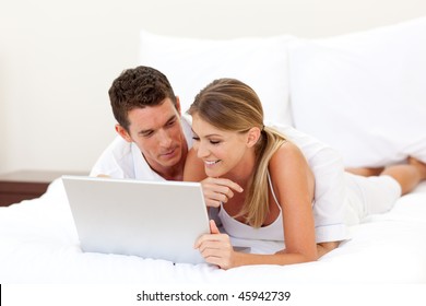 Affectionate couple using a laptop lying on their bed