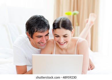 Affectionate couple using a laptop lying on their bed