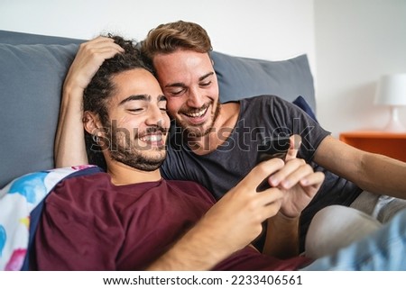 Affectionate gay couple watching content online with mobile cellphone in the bed - homosexual gay people stay together using smartphone - LFTB culture and people lifestyle concept