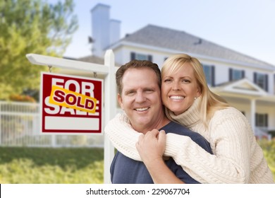 Affectionate Happy Couple In Front Of New House And Sold For Sale Real Estate Sign.