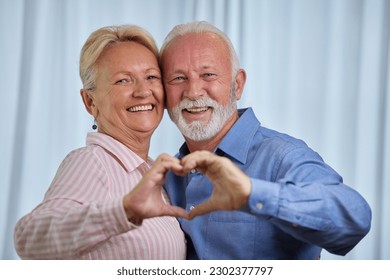 Affectionate happy elderly couple make heart shape gesture with hands. Senior husband and wife looking at camera, bonding and smiling showing symbol of love - Powered by Shutterstock