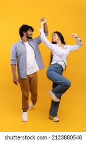 Affectionate indian couple holding hands and dancing together over yellow studio background, having fun and enjoying favourite song, crop