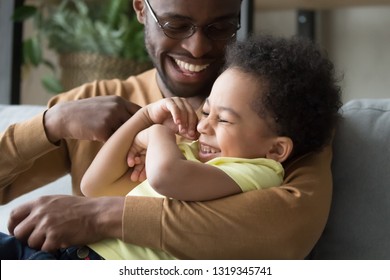 Affectionate Loving African Dad Holding Tickling Child Toddler Son, Happy Playful Black Father And Mixed Race Kid Boy Embracing Having Fun Laughing Cuddling Enjoy Positive Emotions Playing Together