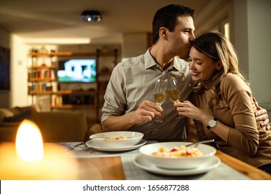 Affectionate man kissing his girlfriend while toasting with Champagne during dinner at dining table.  - Powered by Shutterstock