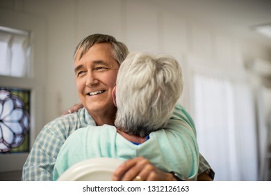 Affectionate Mature Couple Share A Spontaneous Hug As They Finish Putting The Dishes Away.