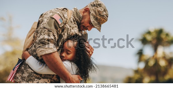 Affectionate military reunion between father\
and daughter. Emotional military dad embracing his daughter on his\
homecoming. Army soldier receiving a warm welcome from his child\
after deployment.