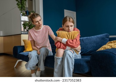 Affectionate mom trying to establish contact with teenage daughter sitting on couch at home. Withdrawn girl turned away from mother, ignores attempts to help. Difficult teenager, problems at school. - Shutterstock ID 2317352383