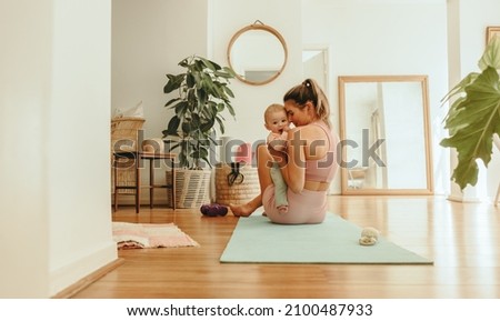 Affectionate mom working out with her baby at home. Healthy mom holding her baby while sitting on an exercise mat. New mom bonding with her baby during her post-natal fitness routine.