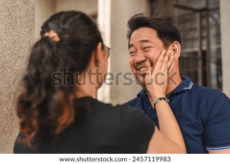 An affectionate moment captured as an Asian woman playfully slaps her smiling husband, showcasing love and playfulness in a middle-aged couple.