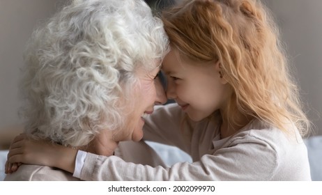 Affectionate Moment. Smiling Little Red Haired Girl Hug Neck Of Mature Retired Grandmother Express Love Gratitude To Beloved Grandparent. Happy Foster Kid And Aged Woman Custodian Embrace Touch Noses