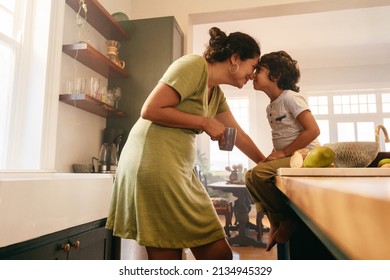 Affectionate mother touching noses with her young son in the kitchen. Cheerful mother and son looking at each other fondly. Loving single mother bonding with her son at home.
