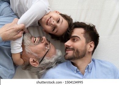 Affectionate Multi Three 3 Generation Men Family Top View Close Up Portrait, Cute Little Kid Grandson Embrace Old Grandfather Looking At Camera Relaxing Laughing With Young Father Enjoy Funny Moments