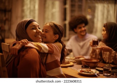 Affectionate Muslim grandmother and granddaughter embracing during family meal in dining room. - Shutterstock ID 2223608311
