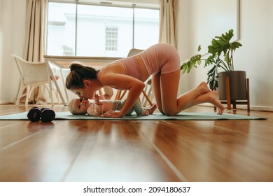 Affectionate New Mom Kissing Her Baby On The Cheek. Yogi Mom Working Out With Her Baby On An Exercise Mat. New Mom Bonding With Her Baby During Her Post-natal Fitness Routine.