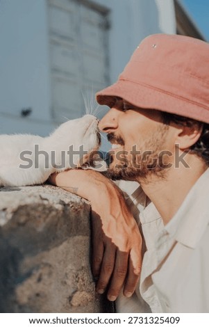 Affectionate Nose Rub Between a Man in a Bucket Hat and a White Cat.