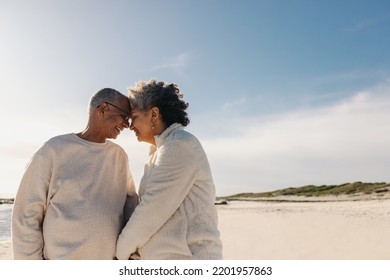 Affectionate Senior Couple Smiling And Touching Their Heads Together At The Beach. Mature Couple Sharing A Romantic Moment Outdoors. Happy Elderly Couple Couple Bonding During Retirement.