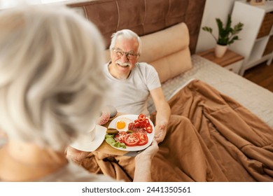 Affectionate senior woman is bringing breakfast in bed to her hungry husband. - Powered by Shutterstock