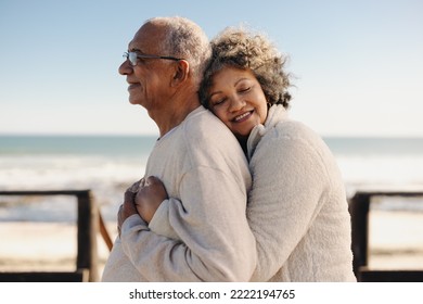 Affectionate senior woman smiling happily while embracing her husband by the ocean. Romantic elderly couple enjoying spending some quality time together after retirement. - Powered by Shutterstock