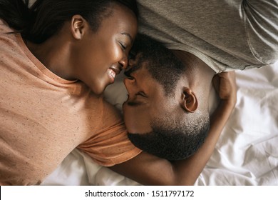 Affectionate young African American couple lovingly kissing while lying face to face in bed together in the morning - Powered by Shutterstock