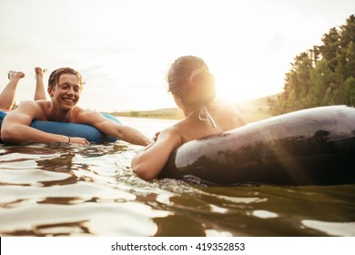 Affectionate Young Couple Floating On Inner Tubes In Water. Young Man And Woman In An Inflatable Tube In A Lake On A Sunny Day.