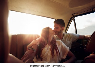 Affectionate young couple sitting in back seat of a car. Young man and woman in rear seat of a vehicle kissing.
