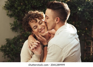 Affectionate young man kissing his girlfriend outdoors. Romantic young man kissing his girlfriend on the cheek while embracing her. Young LGBTQ+ couple spending quality time together. - Shutterstock ID 2041289999