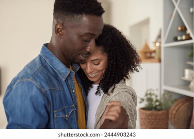 Affectionate young multiracial couple smiling and dancing arm in arm together in their comfortable kitchen at home - Powered by Shutterstock