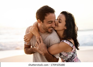 Affectionate young woman hugging her husband while having fun together on a sandy beach at sunset - Shutterstock ID 1709105680