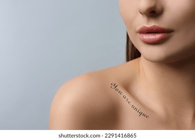 Affirmation. Woman with tattooed phrase You Are Unique on collarbone against light grey background, closeup. Space for text
