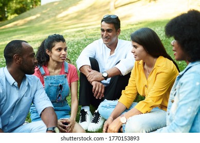 Afghan, black, mexican and indian chatting while sitting in the park on the grass. The concept of communication of different nationalities. Diverse people and friends