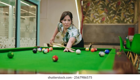 Afghan happy young adult gen z alone business woman hold cue stick hit ball play billiards snooker game office after work. Teen age female corporate enjoy break time have fun joy indoor job place - Powered by Shutterstock