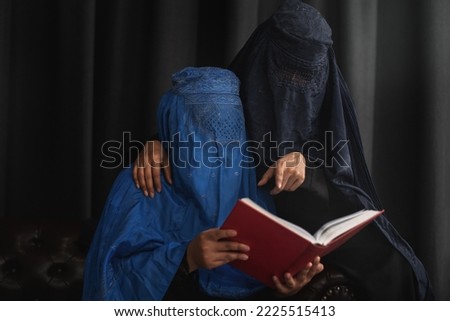 Afghan Muslim women with burka traditional costume, reading holy  Quran against the dark background 
