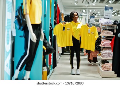 Afican american women in tracksuits shopping at sportswear mall against shelves. She choose yellow t-shirt. Sport store theme. - Powered by Shutterstock