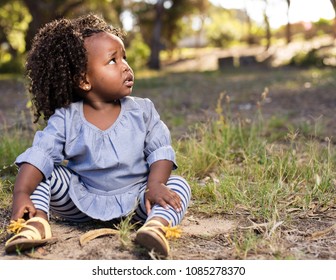 Afican Toddler Sitting Down With A Worried Expression On Her Face.